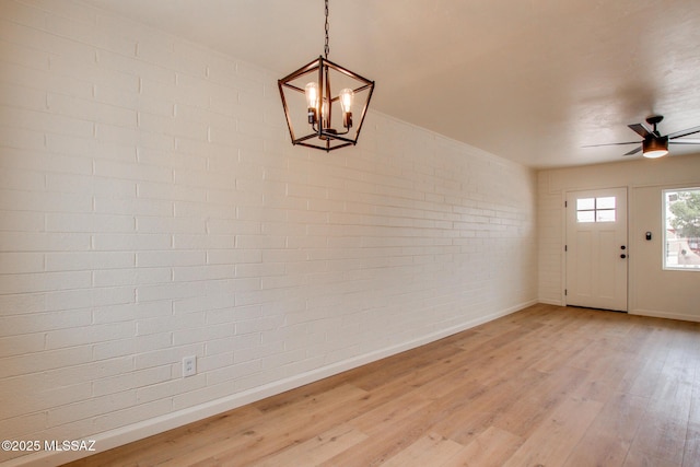 foyer entrance featuring brick wall, baseboards, light wood-style flooring, a chandelier, and ceiling fan
