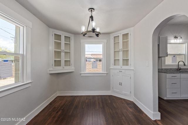 2956 N Tyndall Ave, Tucson, AZ 85719 - unfurnished dining area with arched walkways, dark wood-style flooring, a sink, a chandelier, and baseboards