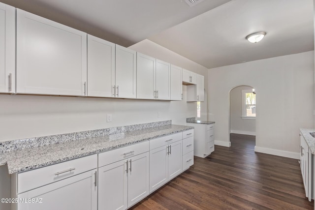 2956 N Tyndall Ave, Tucson, AZ 85719 - kitchen featuring arched walkways, baseboards, dark wood-type flooring, white cabinetry, and light stone countertops