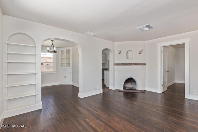 2956 N Tyndall Ave, Tucson, AZ 85719 - unfurnished living room with wood-type flooring, baseboards, a fireplace with raised hearth, arched walkways, and a chandelier