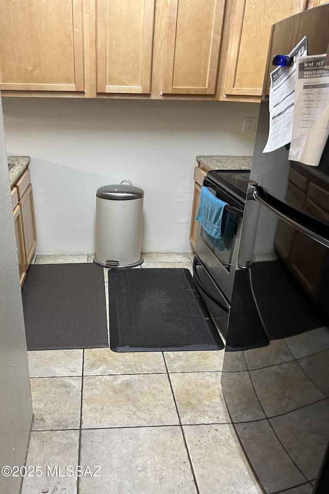 kitchen with freestanding refrigerator, stainless steel electric range oven, tile patterned flooring, light countertops, and light brown cabinetry