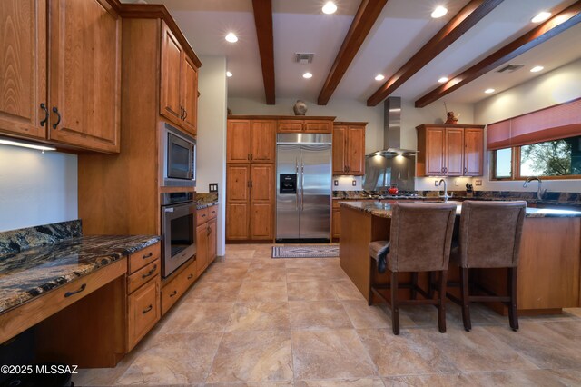 12800 W Arivaca Rd, Amado, AZ 85645 - kitchen featuring built in appliances, wall chimney exhaust hood, brown cabinetry, a kitchen bar, and beam ceiling