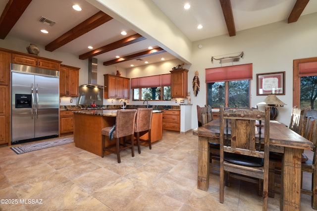 12800 W Arivaca Rd, Amado, AZ 85645 - kitchen with built in fridge, wall chimney range hood, beamed ceiling, brown cabinets, and a breakfast bar