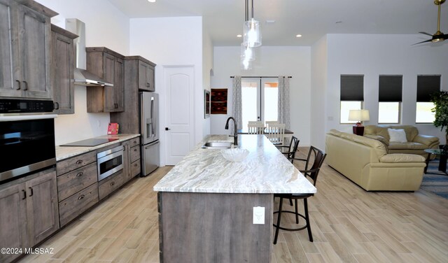 432 N Heritage Point Pl, Sahuarita, AZ 85629 - kitchen with stainless steel appliances, a sink, a kitchen bar, wall chimney range hood, and light wood-style flooring