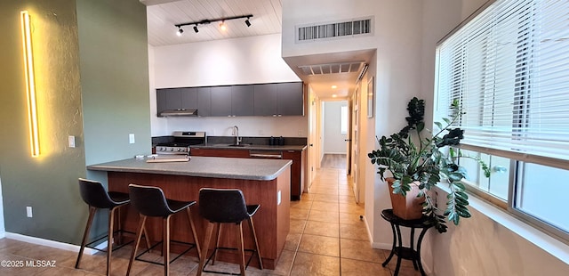 kitchen featuring stainless steel gas stove, a sink, a breakfast bar, light tile patterned floors, and plenty of natural light