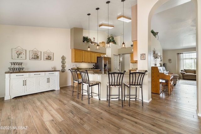 9429 N Elan Ln, Tucson, AZ 85742 - kitchen with stainless steel fridge with ice dispenser, arched walkways, light wood finished floors, a peninsula, and a breakfast bar area