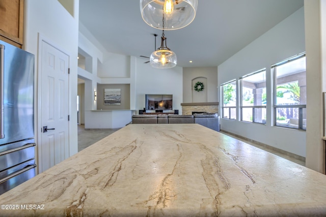 218 W Milbrae Springs Dr, Oro Valley, AZ 85755 - kitchen with freestanding refrigerator, a fireplace, light stone countertops, brown cabinetry, and hanging light fixtures
