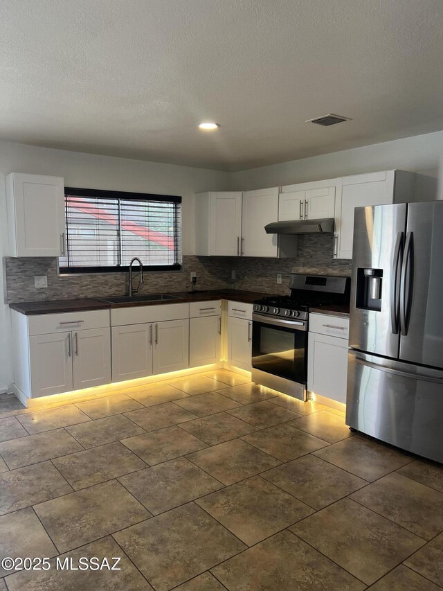 1558 E Los Cabos Pl, Tucson, AZ 85706 - kitchen with stainless steel appliances, under cabinet range hood, dark countertops, tasteful backsplash, and a textured ceiling
