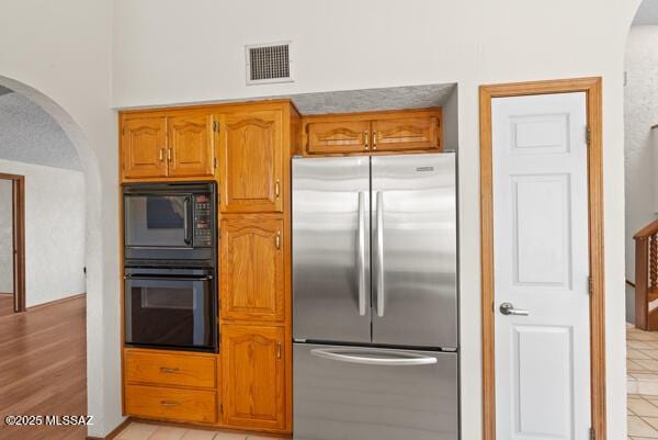 1861 N Camino Claveles, Tucson, AZ 85745 - kitchen featuring stainless steel refrigerator, arched walkways, black microwave, and brown cabinetry