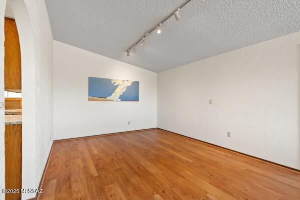1861 N Camino Claveles, Tucson, AZ 85745 - empty room with rail lighting, a textured ceiling, wood finished floors, and arched walkways