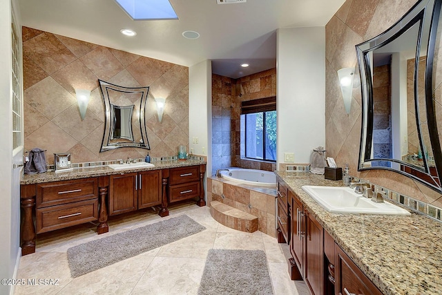 full bathroom featuring tile walls, a skylight, a garden tub, two vanities, and recessed lighting