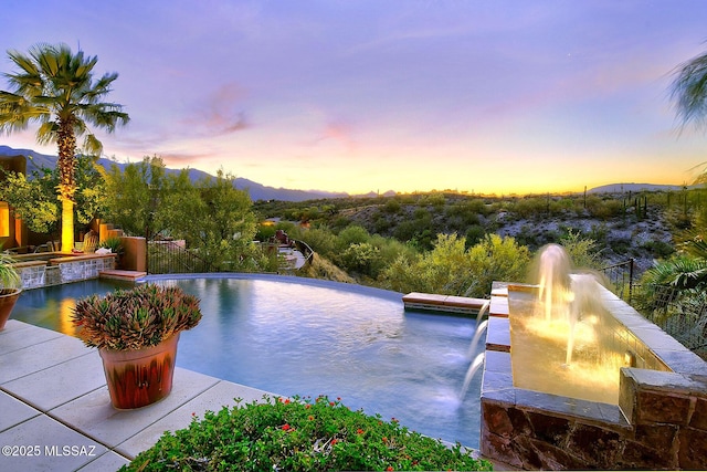 pool at dusk with a pool with connected hot tub and a mountain view
