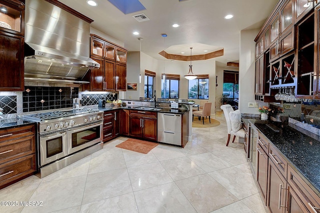kitchen with stainless steel appliances, a peninsula, wall chimney exhaust hood, tasteful backsplash, and dark stone counters