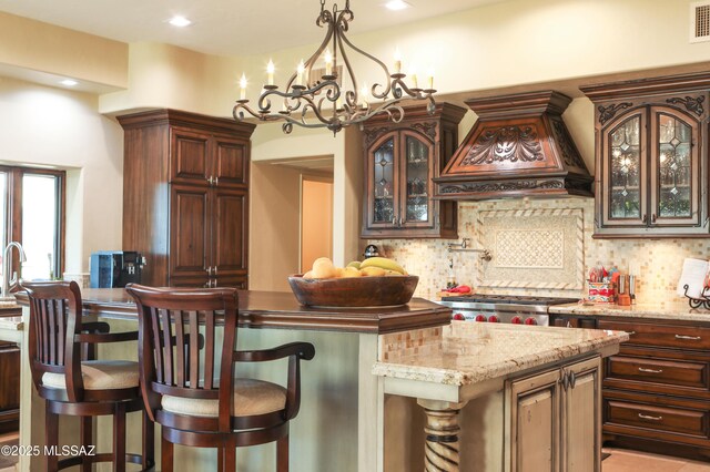 9971 N Desert Sky Rd, Oro Valley, AZ 85737 - kitchen featuring custom exhaust hood, decorative backsplash, a kitchen bar, glass insert cabinets, and a chandelier