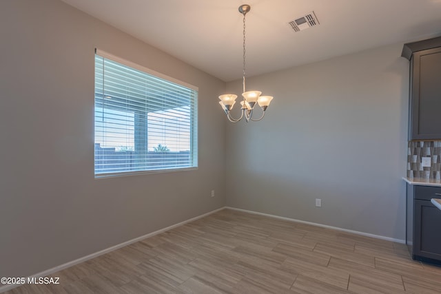 9734 E Miller Peak Trl, Tucson, AZ 85747 - unfurnished dining area with a chandelier, light wood-style flooring, and baseboards