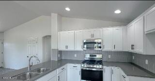 kitchen featuring appliances with stainless steel finishes, lofted ceiling, a sink, white cabinets, and a peninsula