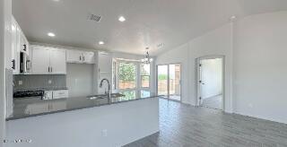 kitchen featuring a peninsula, recessed lighting, white cabinetry, vaulted ceiling, and a sink