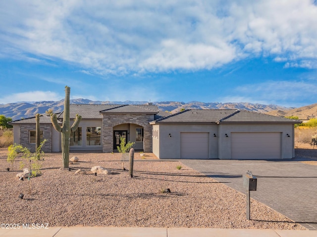 view of front of house with a mountain view, driveway, stone siding, an attached garage, and stucco siding