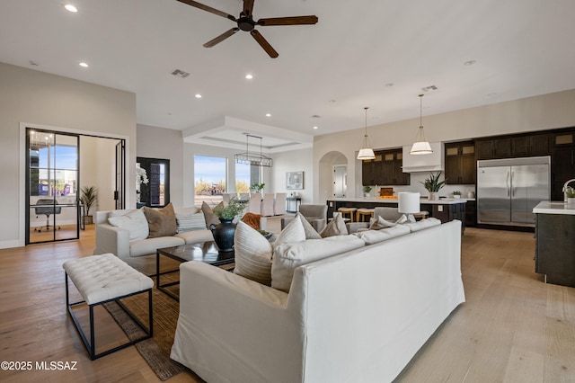 living area with arched walkways, a ceiling fan, light wood-style flooring, and recessed lighting