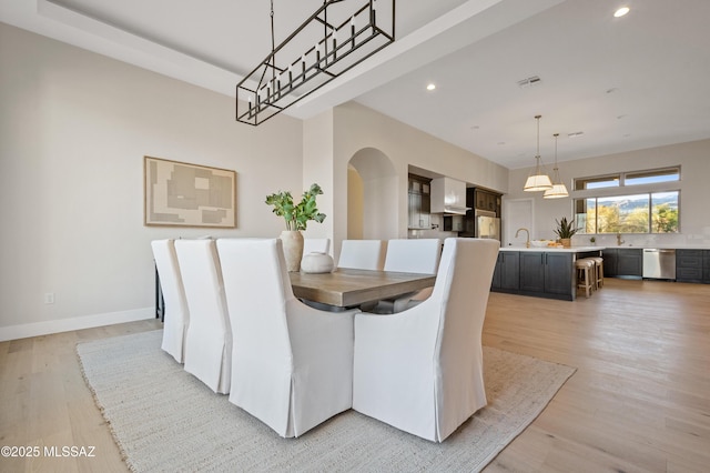 dining area featuring arched walkways, light wood finished floors, recessed lighting, and baseboards