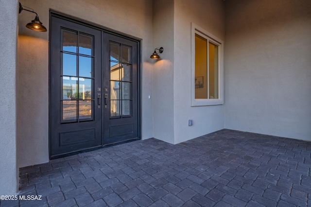 view of exterior entry featuring french doors, stucco siding, and a patio area