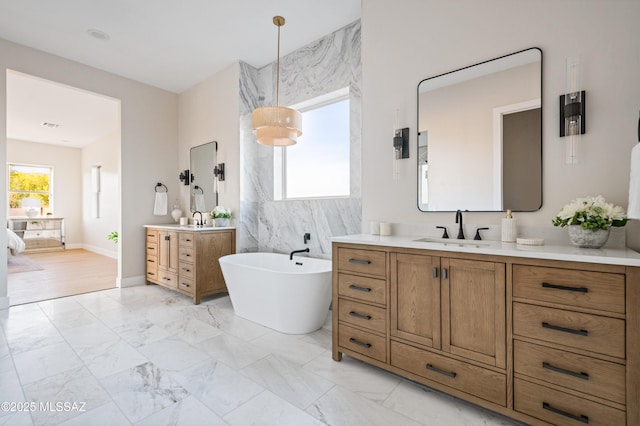 full bath with marble finish floors, a freestanding bath, two vanities, and baseboards
