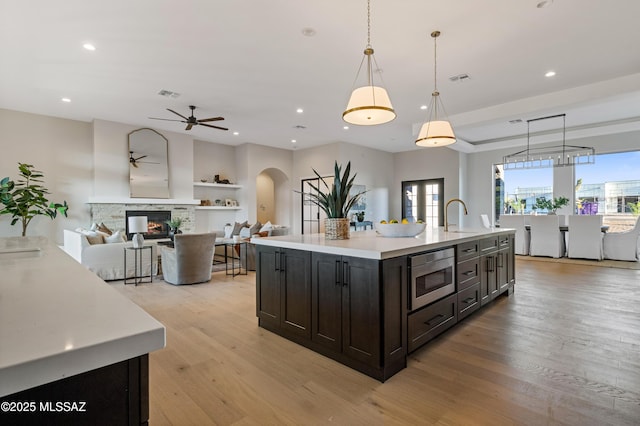 kitchen with arched walkways, a ceiling fan, light countertops, a sink, and light wood-style flooring