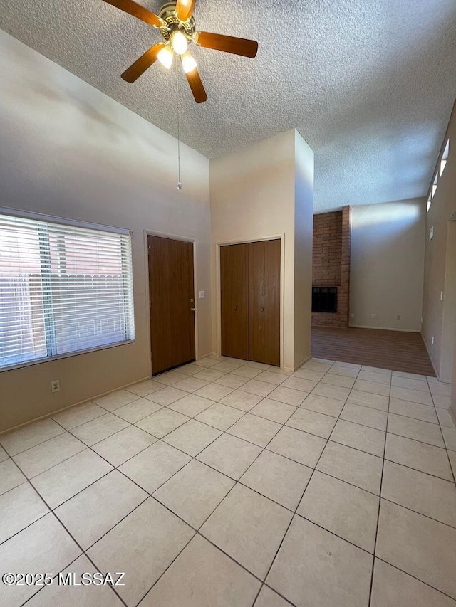 3873 N Pasatiempo Pl, Tucson, AZ 85705 - empty room with a textured ceiling, a fireplace, a ceiling fan, light tile patterned floors, and a towering ceiling