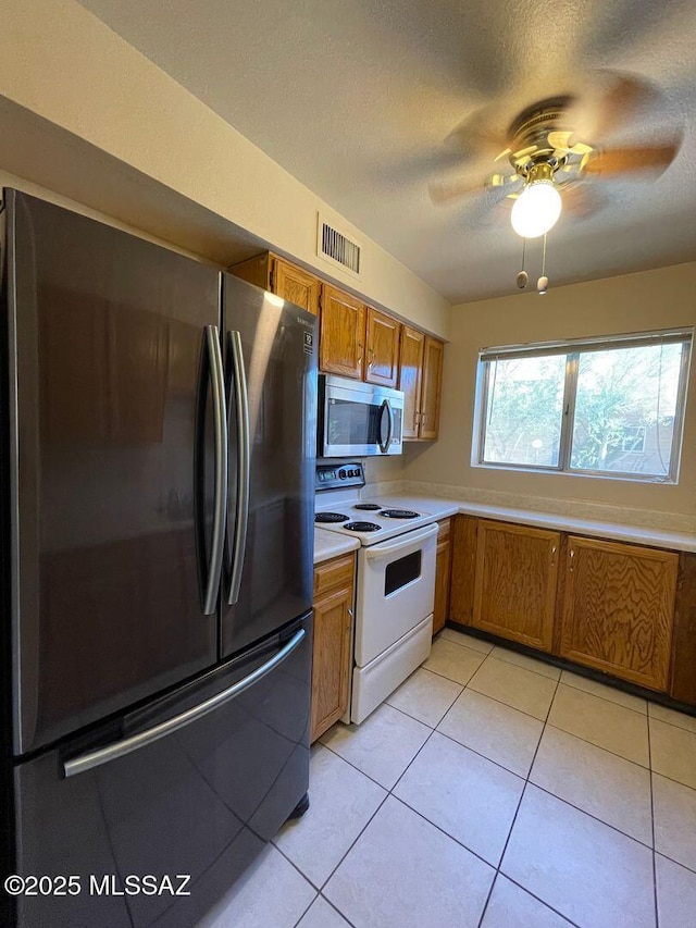 3873 N Pasatiempo Pl, Tucson, AZ 85705 - kitchen featuring freestanding refrigerator, stainless steel microwave, electric range, brown cabinets, and light countertops