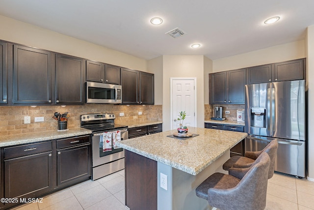10487 S Cutting Horse Dr, Vail, AZ 85641 - kitchen featuring stainless steel appliances, light tile patterned floors, a kitchen island, a kitchen bar, and light stone counters