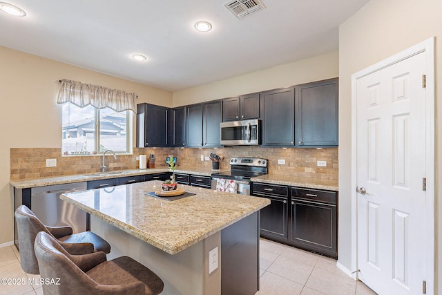 10487 S Cutting Horse Dr, Vail, AZ 85641 - kitchen with appliances with stainless steel finishes, a sink, a kitchen bar, light tile patterned floors, and light stone counters