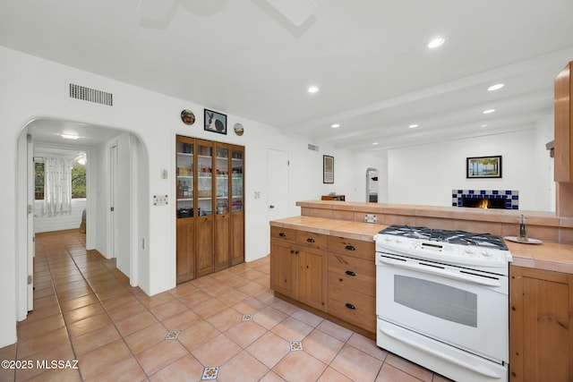 4921 E Camino De Los Olivos, Tucson, AZ 85718 - kitchen featuring white gas range oven, tile counters, light tile patterned floors, arched walkways, and recessed lighting