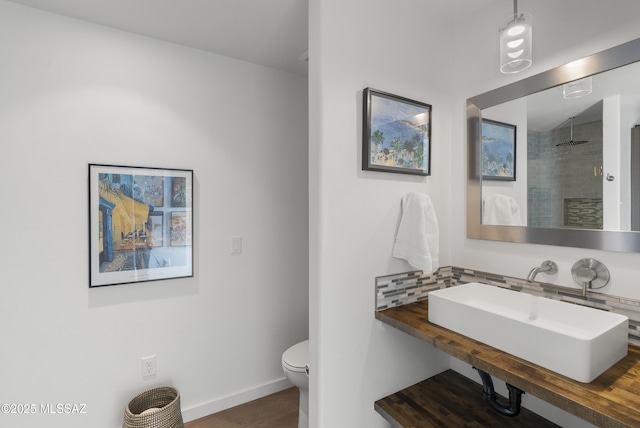 full bath with a sink, baseboards, toilet, decorative backsplash, and tiled shower