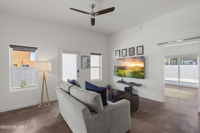 living area featuring finished concrete floors, a ceiling fan, and baseboards