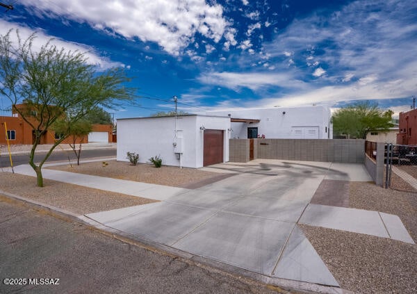 view of front of house with an attached garage, fence, concrete driveway, and stucco siding