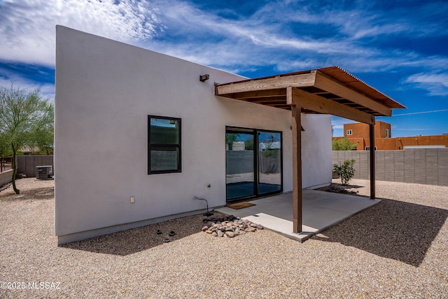 rear view of house featuring stucco siding, central air condition unit, fence, and a patio