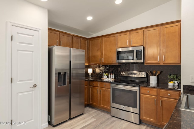 12356 N Globe Mallow Pl, Marana, AZ 85658 - kitchen featuring appliances with stainless steel finishes, brown cabinetry, backsplash, light wood-style flooring, and vaulted ceiling