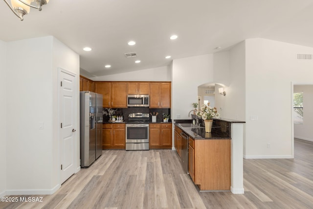 12356 N Globe Mallow Pl, Marana, AZ 85658 - kitchen featuring appliances with stainless steel finishes, lofted ceiling, arched walkways, brown cabinetry, and light wood-style flooring