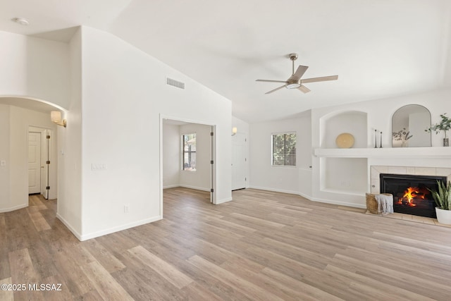 12356 N Globe Mallow Pl, Marana, AZ 85658 - unfurnished living room featuring a ceiling fan, light wood-type flooring, a tile fireplace, arched walkways, and high vaulted ceiling