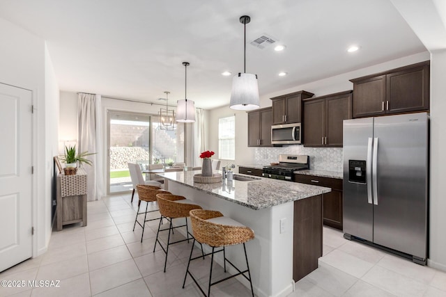 6633 E Paseo De Sambuca, Tucson, AZ 85756 - kitchen with stainless steel appliances, dark brown cabinetry, light stone countertops, backsplash, and an island with sink