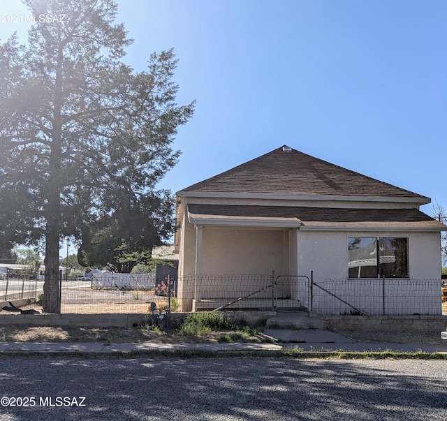 view of front of home with a gate, stucco siding, a fenced front yard, and roof with shingles