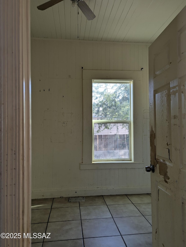 unfurnished room featuring light tile patterned floors, ceiling fan, and wooden walls