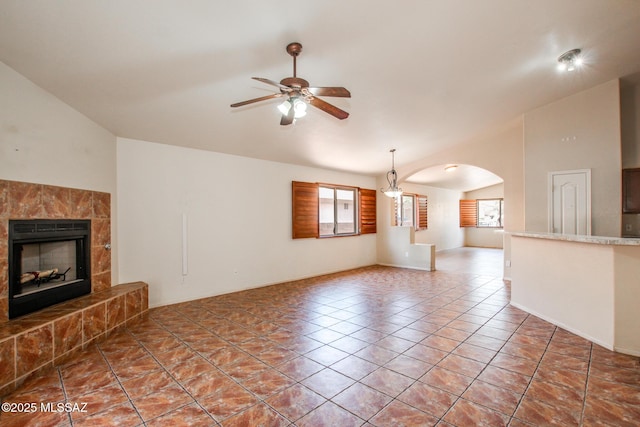8145 E Smooth Sumac Ln, Tucson, AZ 85710 - unfurnished living room with ceiling fan, vaulted ceiling, arched walkways, and a tiled fireplace