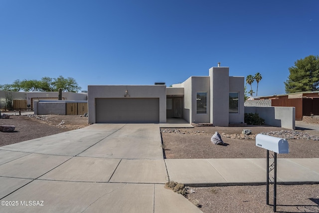 pueblo-style home with stucco siding, a garage, and concrete driveway