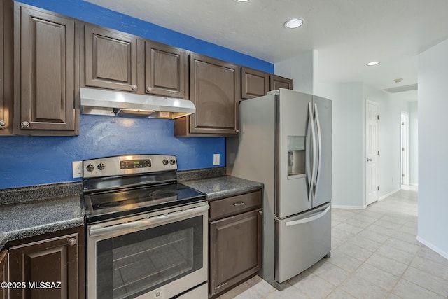 kitchen featuring stainless steel appliances, under cabinet range hood, dark countertops, light tile patterned floors, and dark brown cabinetry