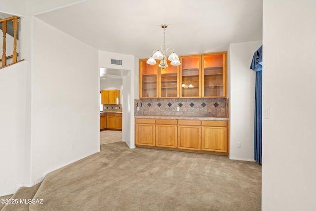12220 E 5th St, Tucson, AZ 85748 - kitchen with light colored carpet, a chandelier, brown cabinets, decorative backsplash, and glass insert cabinets