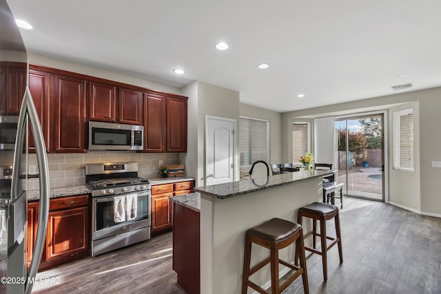 10676 S Miramar Canyon Pass, Vail, AZ 85641 - kitchen with stainless steel appliances, dark wood-style flooring, decorative backsplash, a breakfast bar area, and light stone countertops