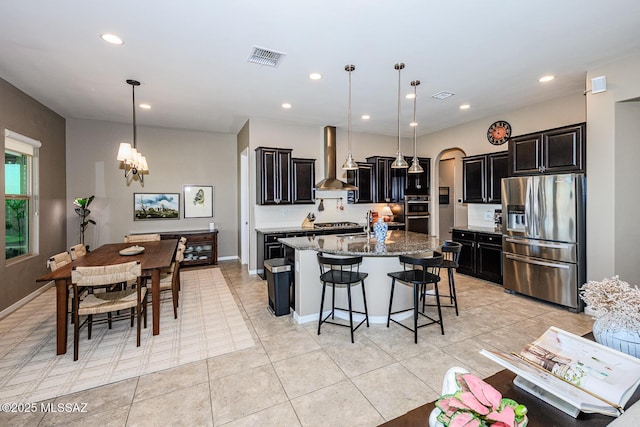 4762 W Placita Casa Sevilla, Marana, AZ 85658 - kitchen with stainless steel appliances, wall chimney range hood, a center island with sink, a kitchen breakfast bar, and a chandelier