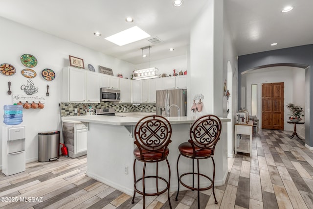 8434 N Sunny Rock Ridge Dr, Tucson, AZ 85743 - kitchen featuring appliances with stainless steel finishes, arched walkways, a breakfast bar, light wood finished floors, and recessed lighting