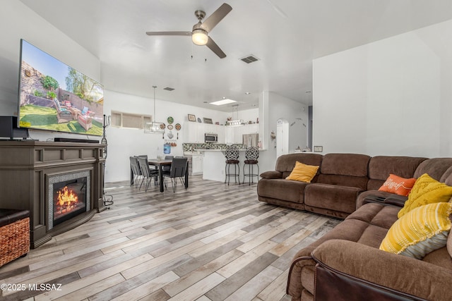 8434 N Sunny Rock Ridge Dr, Tucson, AZ 85743 - living area with light wood-style floors, ceiling fan, and a lit fireplace